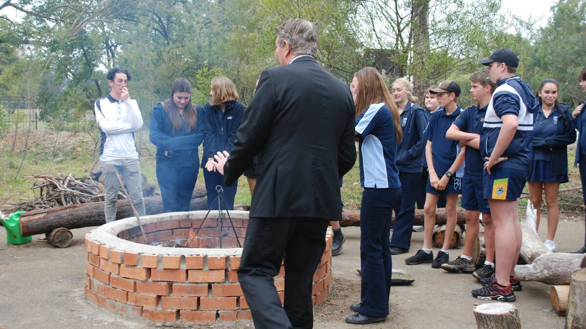 Minister Ray Williams warms his hand with students at the fire pit at Birriban, the Aboriginal cultural site on the school grounds.