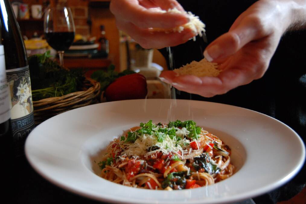 Rachel Roberts drizzles parmesan cheese over a traditional Italian pasta featuring fresh herbs, garden vegetables and posata pomodoro.