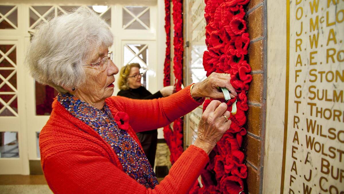 Blue Mountains Hospital Auxiliary member, Paula Savage, adds ribbons bearing the names of staff members' relatives to the poppy wall.
