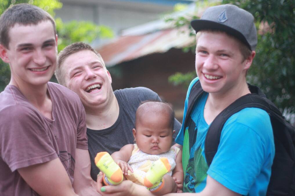 From left, Hamish Cullen, James Hodge and Tom Farnell with a baby in Indonesia. Photo: Michael McClean.