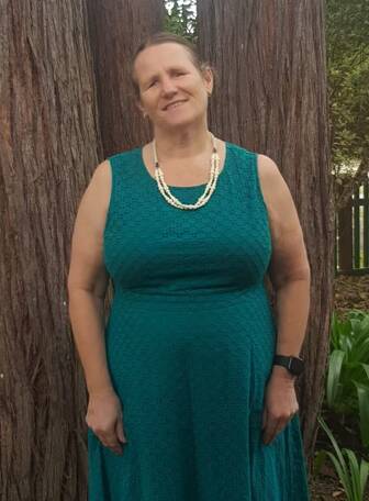 A woman standing in front of a tree wearing a green dress smiling: Glenbrook resident Fiona Woods is the new president of Blind Citizens Australia.