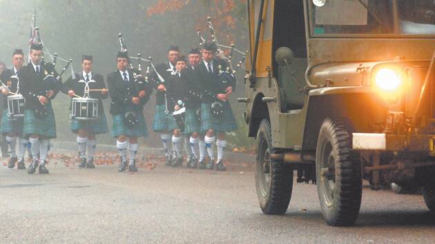 A replica vintage army jeep's headlights guide the Blue Mountains Pipe Band through thick fog during the Anzac Day march towards the cenotaph at Honour Avenue, Lawson.