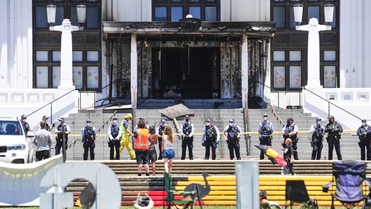 Protesters stand in front of the burned out entrance doors to Old Parliament House in Canberra. Picture: Dion Georgopoulos