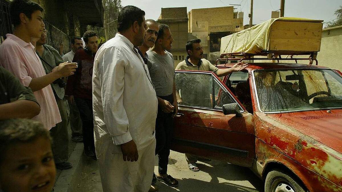 Iraqi men and children stop near a car carrying the body of a civilian killed the night before in a shelling in Baghdad, Iraq. 20th April, 2003. Photo: Kate Geraghty