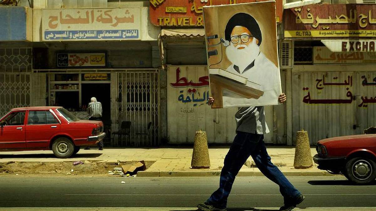 An Iraqi man walks along a Baghdad street holding a painting of Grand Ayatollah Mohammad Mohammad Sadeq al-Sadr, the father of Moqtada Al-Sadr. Saddam murdered him. Baghdad, Iraq. March 2003. Photo: Kate Geraghty