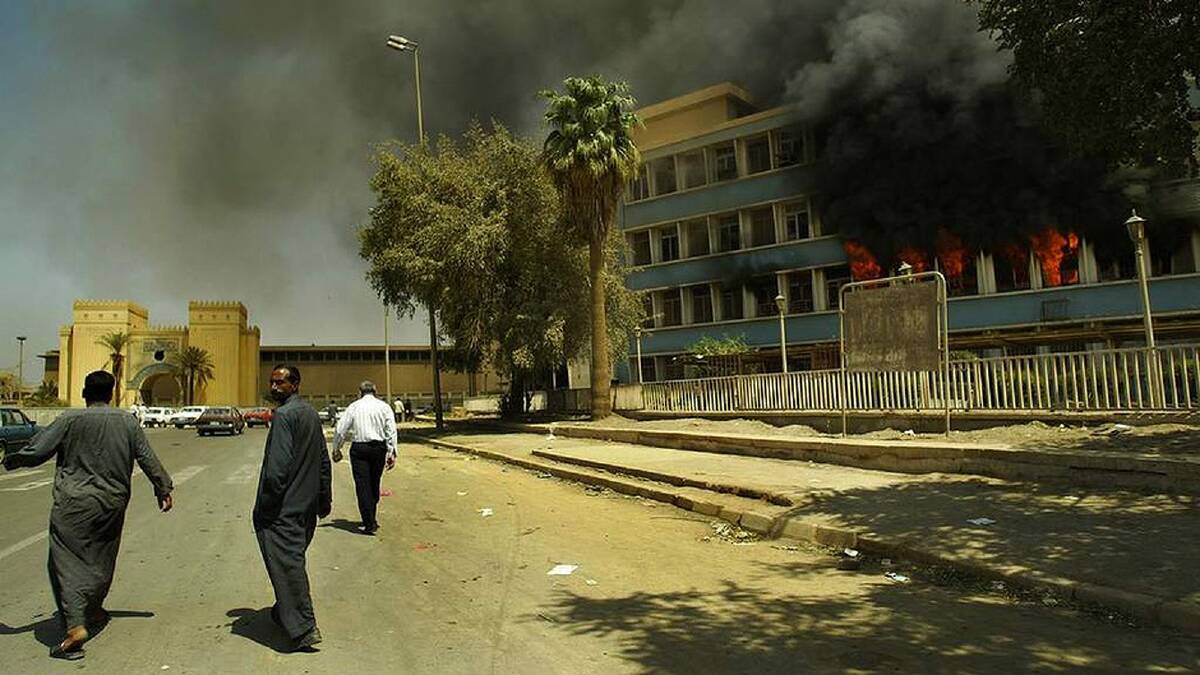 Iraqi men walk past a government building on fire in Baghdad, Iraq. March, 2003. Photo: Kate Geraghty
