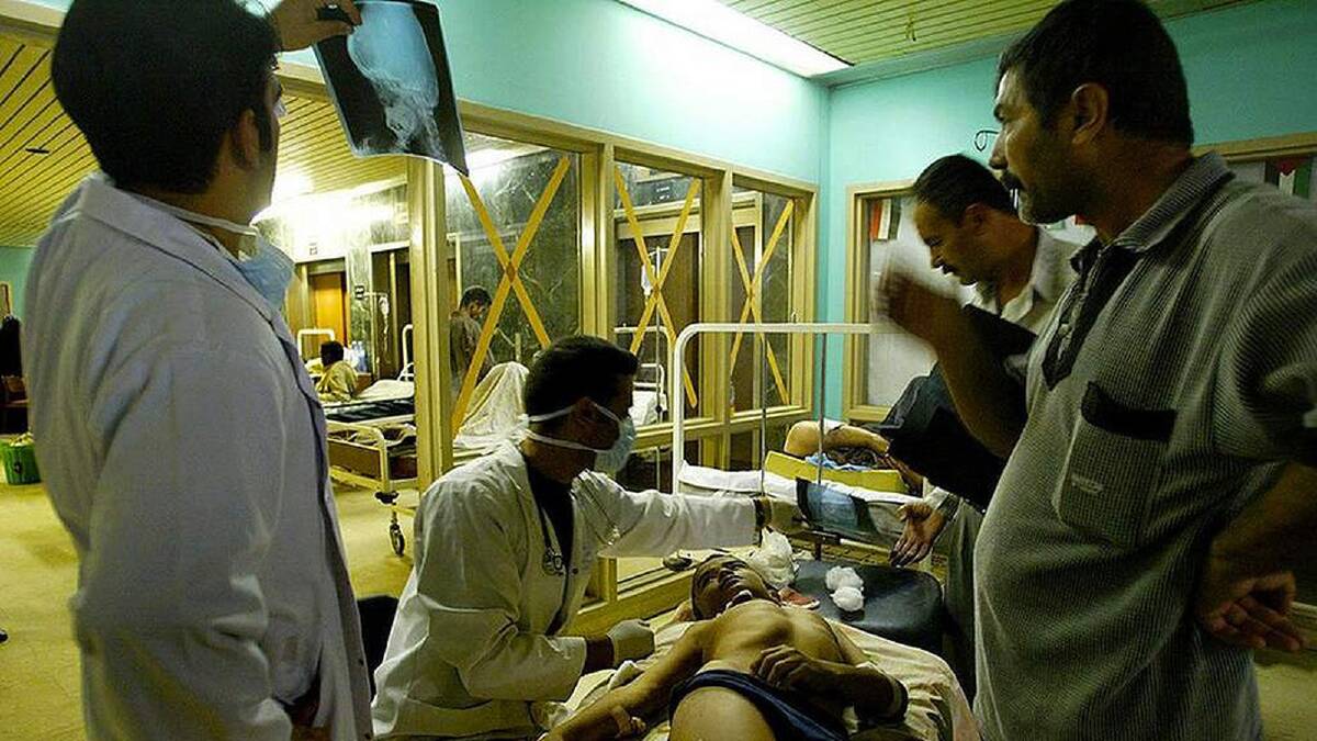 A doctor examines the x-ray showing shrapnel before treating the young boy with multiple injuries as he is comforted by his father and uncle at a hospital in Baghdad, Iraq. 29th March, 2003. Photo: Kate Geraghty