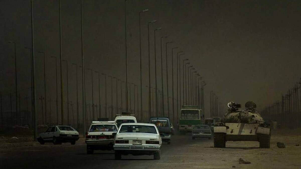 Iraqi civilians heading out of Umm Qsar pass British tanks as they drive towards Basra after hearing of the fall of Basra. Thick clouds of smoke coming from the battle of Basra masks the sky. 7th April, 2003. Photo: Kate Geraghty
